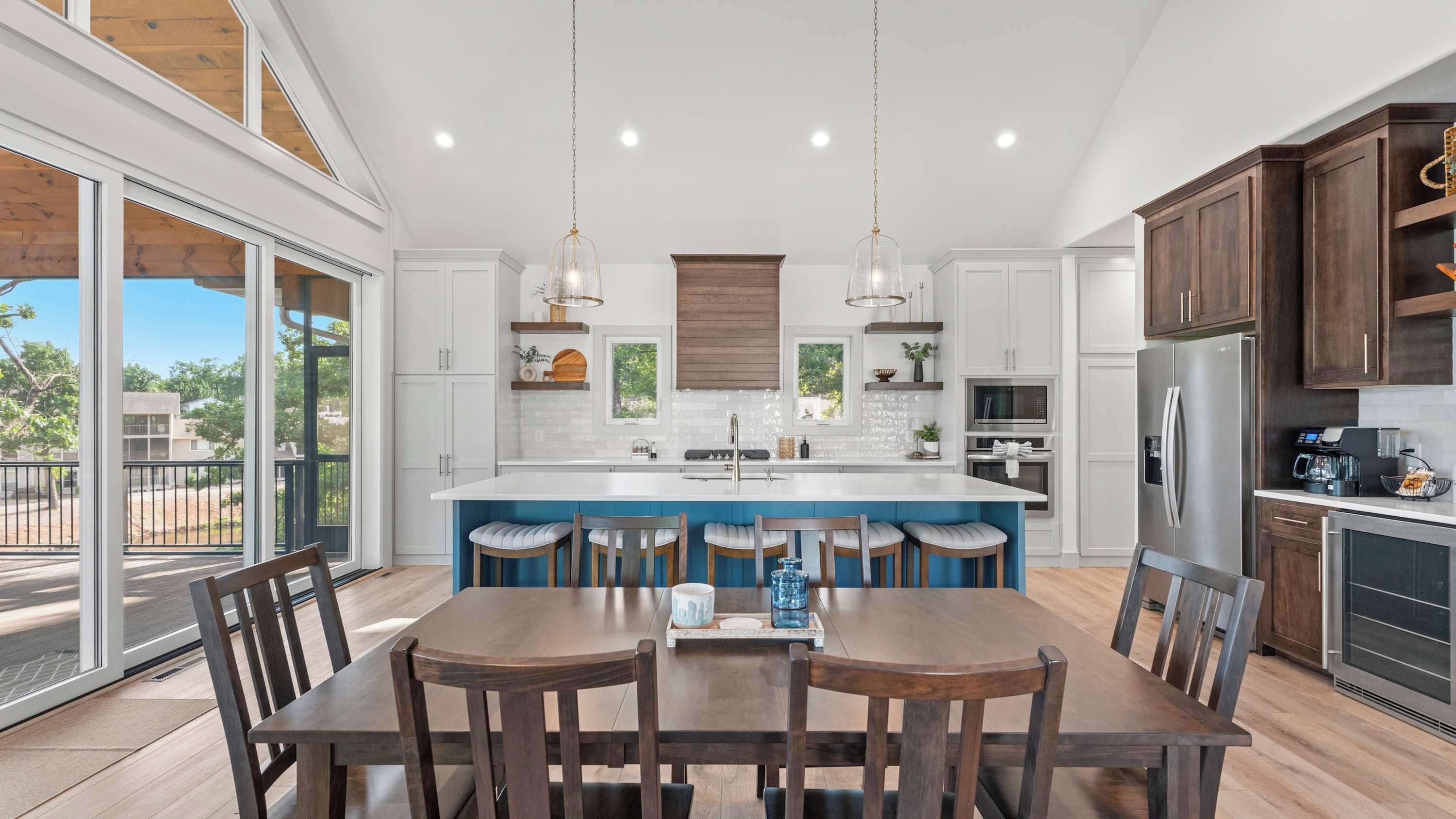 A modern kitchen with a central island, bar stools, and a dining table with chairs.