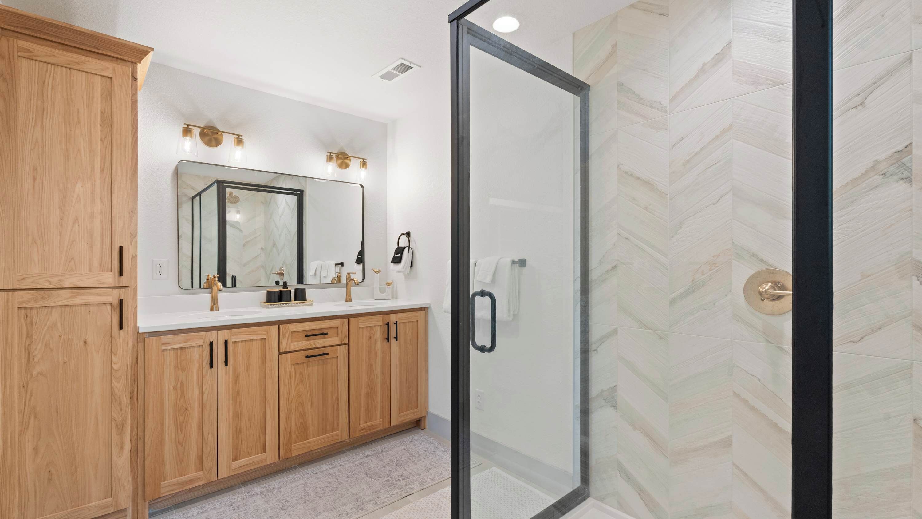 A modern bathroom with wooden cabinets, a large mirror, and a glass shower enclosure.