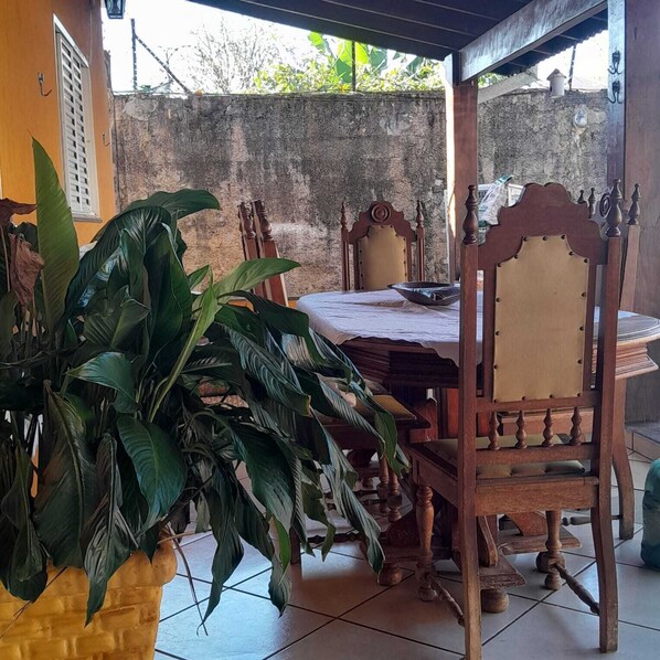 A room with a bed, a wooden chair, a table, and a large potted plant.