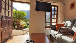 A living room with a sofa, a television, a window with a view of mountains, and a plant. - Casa Lara Hermigua - Studio ESTAMBUL with terrace - Ideal for families (Hermigua)