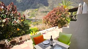 A table set for two with a bottle of wine, two plates, and two glasses, overlooking a mountainous landscape. - Casa Lara Hermigua - Studio ESTAMBUL with terrace - Ideal for families (Hermigua)