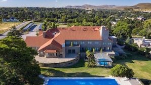 Ett stort hus med en swimmingpool, omgivet av grönska och kullar.