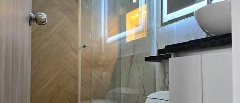 Et moderne badeværelse med en glasbrusekabine, et hvidt toilet og en vask med spejl.