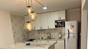 A modern kitchen with a marble island, black bar stools, hanging utensils, and a refrigerator. - Casa completa 2 habitaciones 2 baños a 7 minutos del aeropuerto y 5 de la ciudad (Guaymallen)
