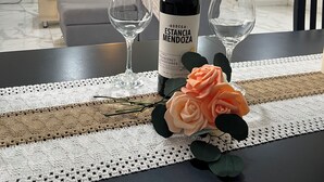 A dining table with a bottle of wine, two wine glasses, and a rose. - Casa completa 2 habitaciones 2 baños a 7 minutos del aeropuerto y 5 de la ciudad (Guaymallen)
