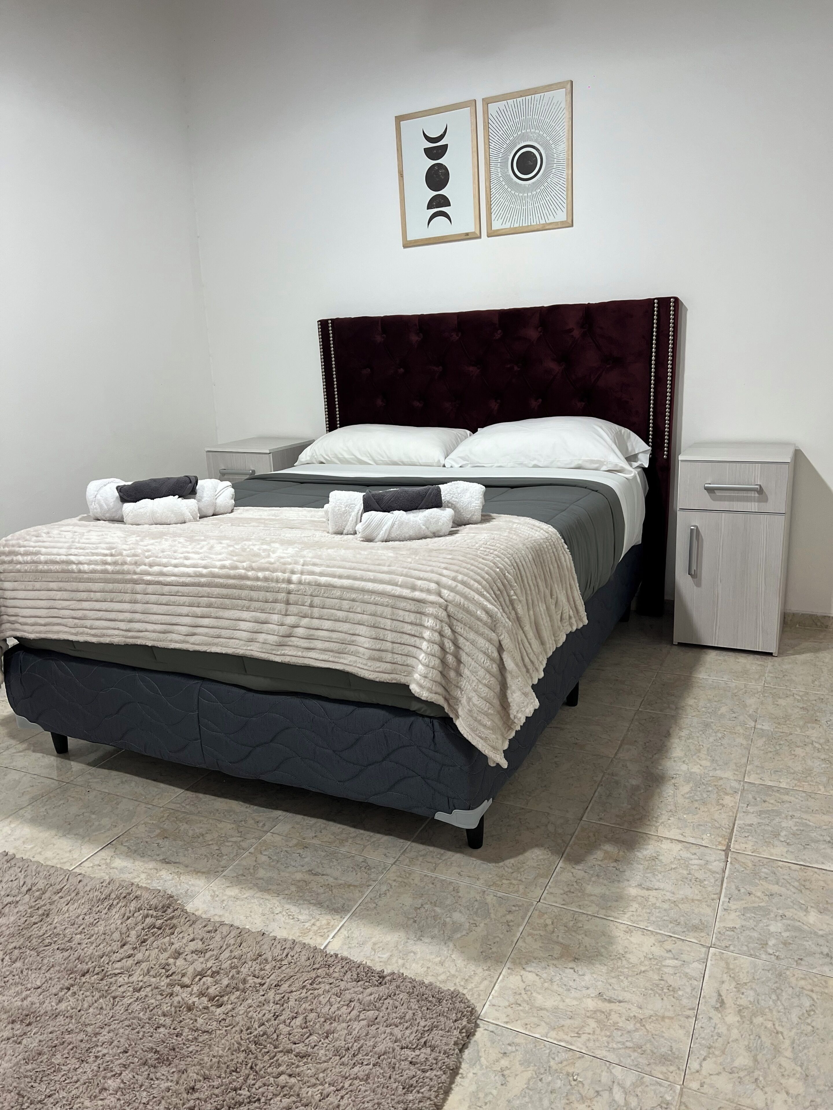 A neatly made bed with a dark headboard, a bedside table, and a small cabinet.
