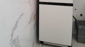 Ein weißer Kühlschrank mit einer schwarzen Unterschublade, vor einer Wand mit Marmoroptik platziert.