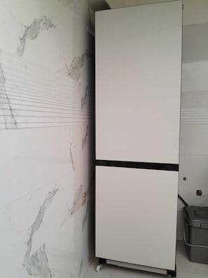 Ein weißer Kühlschrank mit einer schwarzen Unterschublade, vor einer Wand mit Marmoroptik platziert.
