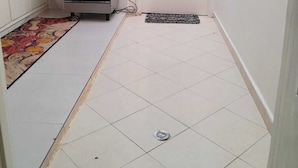 Eine kleine Küche mit Gasherd, Backofen, weißen Schränken, Fliesenboden und einem Fenster mit Vorhängen.