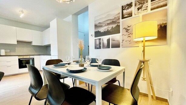 A modern dining area with a white table set for four, black chairs, a vase with dried flowers, and a floor lamp. - Leemstraat Chic Escape for Four (Antwerp)