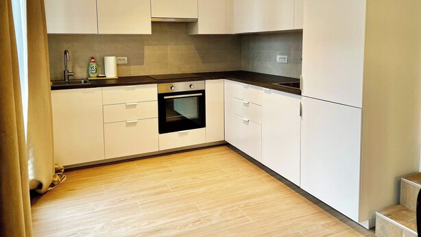 Een moderne keuken met witte kastjes, een zwarte oven en een houten vloer.