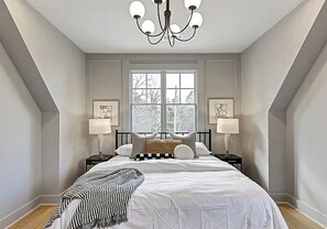 Ein Schlafzimmer mit einem großen Bett, zwei Nachttischen, einer Chandelier und einem Fenster.
