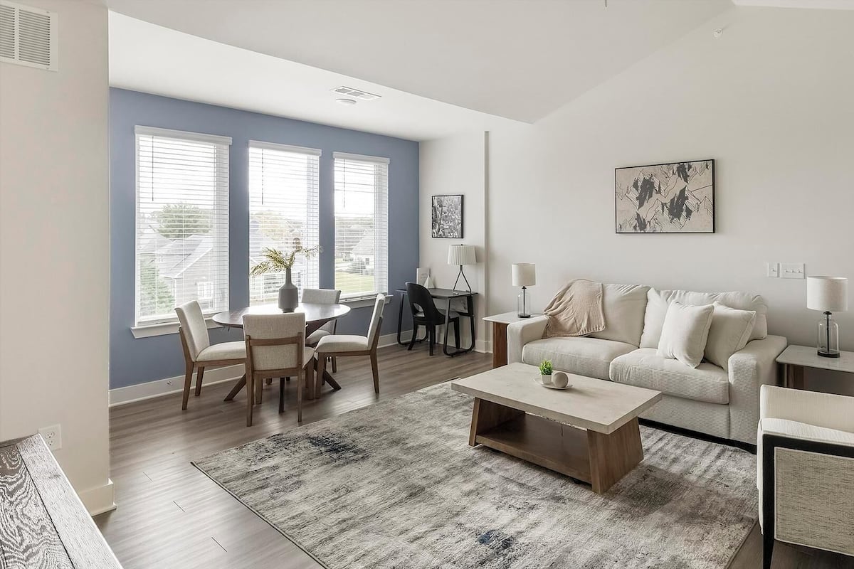 A modern living room with a dining area, a sofa set, a coffee table, and a large window with blinds.