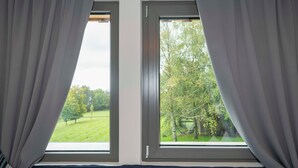 Duas janelas com cortinas, vista para uma paisagem verde e parede com padrão.