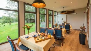 Uma sala de jantar com grandes janelas, piso de madeira e cadeiras estofadas em azul.