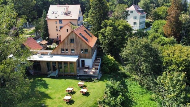 Um edifício grande com vários andares, uma área externa coberta e um gramado com mesas e cadeiras.
