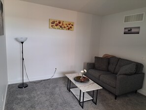 Un salon avec un canapé gris, une table basse blanche, un lampadaire et un tableau représentant des fleurs accroché au mur.