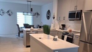 Een moderne keuken met een centraal eiland, roestvrijstalen apparatuur en een zithoek met een bank en stoelen.