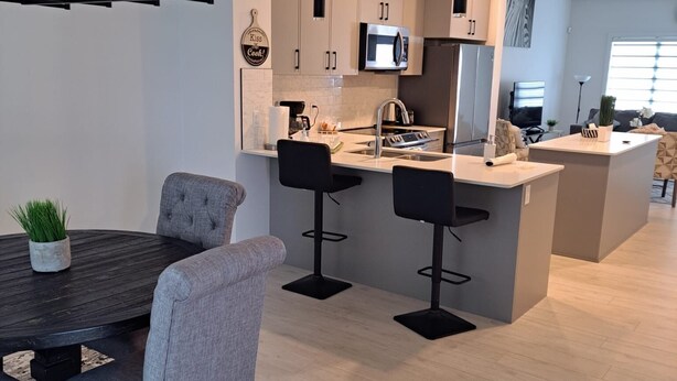 Een moderne keuken met een eethoek, voorzien van een centraal kookeiland, barstoelen en een koffieapparaat.