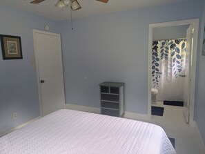 A bedroom with a bed, a wardrobe, a ceiling fan, a door, and a bathroom with a shower curtain. - Quiet Court, Near NAS, Downtown, & Beaches. View of Blue Angels practice! (Pensacola)