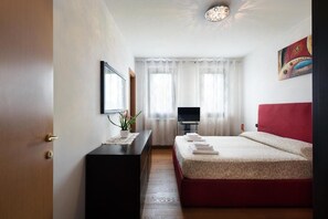 Een hotelkamer met een bed, een bureau met een computer, een televisie en een raam met gordijnen.