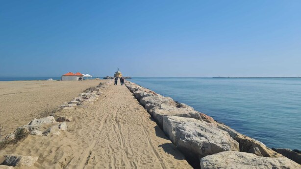 A sandy beach with a rocky breakwater leading to a small structure with a red roof. - La Serenissima: beach, bicycle and Venice !!! (Punta Sabbioni)