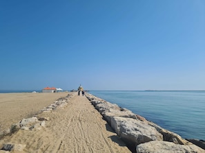A sandy beach with a rocky breakwater leading to a small structure with a red roof. - La Serenissima: Enjoy Venice from the sea—it's easier to get there!!! (Punta Sabbioni)
