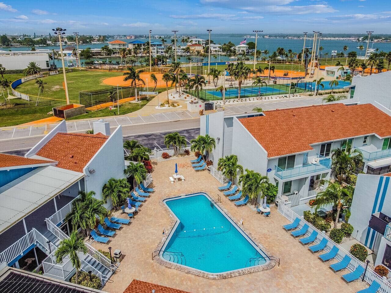 A hotel with a swimming pool, sun loungers, and a view of a sports field.