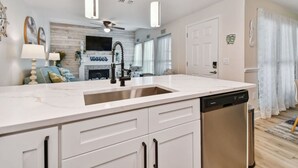 A modern kitchen with a dishwasher, white cabinetry, and a fireplace. - Madeira Beach Yacht Club! Steps to Beach Access! (North Redington Beach)