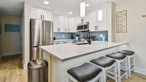 A modern kitchen with white cabinets, stainless steel appliances, a marble island, and bar stools. - Madeira Beach Yacht Club! Steps to Beach Access! (North Redington Beach)