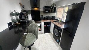 A compact kitchen with a dining area, a washing machine, and a refrigerator. - Comfortable 1-bed Chester Apartment with Parking & Full Kitchen, Home from Home (Chester)
