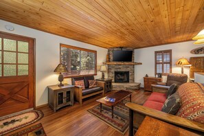 A cozy living room with a stone fireplace, wooden ceiling, and a television mounted above it. - Hot Tub Under the Stars • Trails Out Your Door (Big Bear Lake)