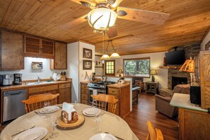 A wooden interior with a dining area, kitchen, and living space, featuring a fireplace and a ceiling fan. - Hot Tub Under the Stars • Trails Out Your Door (Big Bear Lake)