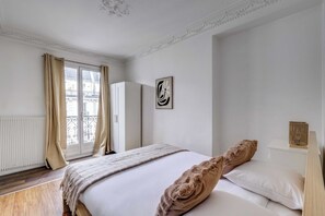 A bedroom with a bed, a window with curtains, a radiator, a wardrobe, and a wall-mounted artwork. - Haussmannian apt - 2bdr/6p Near Marais/sentier (Paris)