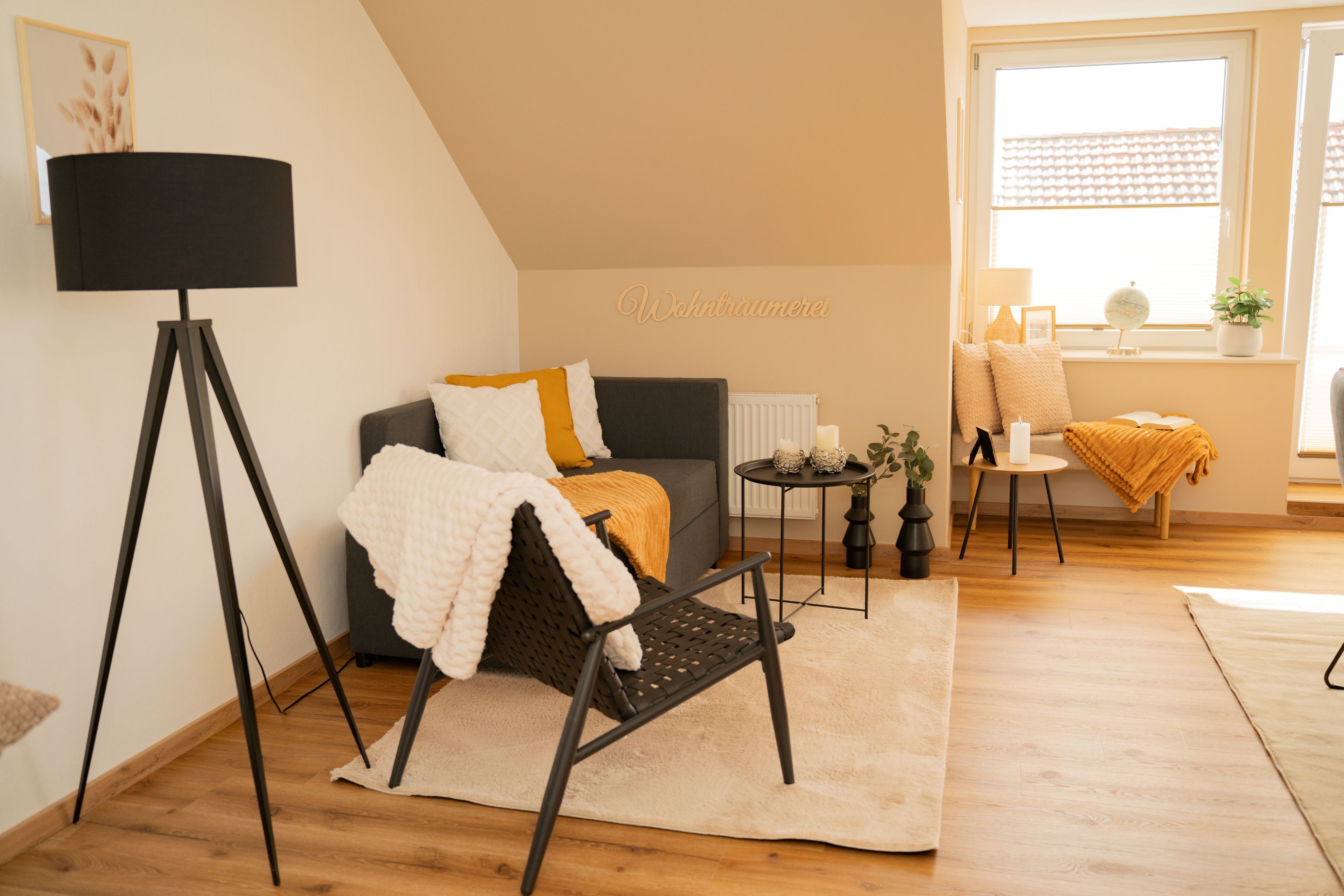 Een gezellige woonkamer met een bank, een fauteuil, een vloerlamp en een klein tafeltje met kaarsen.