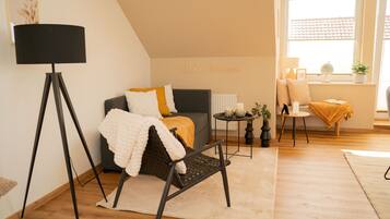 Een gezellige woonkamer met een bank, een fauteuil, een vloerlamp en een klein tafeltje met kaarsen.