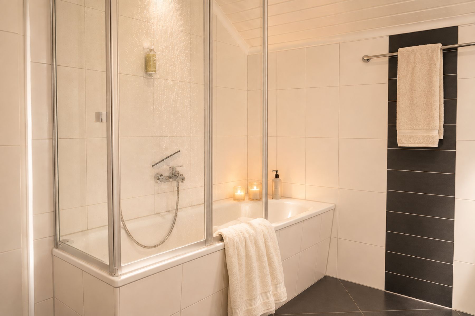 A modern bathroom with a glass-enclosed shower, a white bathtub, and a black tiled wall.