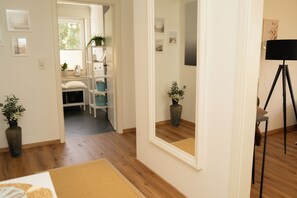 Une pièce avec un plancher en bois, un lit, un miroir, une lampe et une porte qui donne sur une autre pièce.