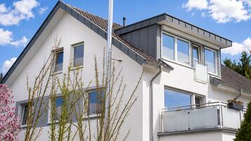 Ein modernes, zweistöckiges Haus mit Balkon, großen Fenstern und blauem Himmel.