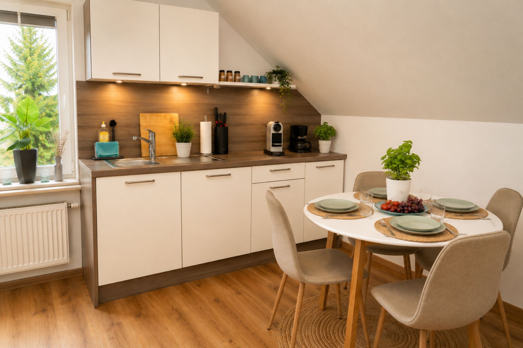 A modern kitchen with a dining area, wooden flooring, and a view of greenery outside.