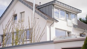 Une maison moderne à deux étages, dotée d’un toit en pente, de grandes fenêtres et d’un balcon.