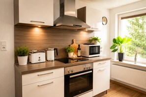 A modern kitchen with a built-in oven, microwave, and toaster. There are plants on the counter and a window with a view of greenery. - Arrive & Feel at Home • Fireplace • calm • Parking Lot (Paderborn)