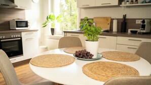 Une cuisine moderne avec une table à manger ronde, des sets de table en fibres naturelles, une plante en pot et un saladier de raisins.