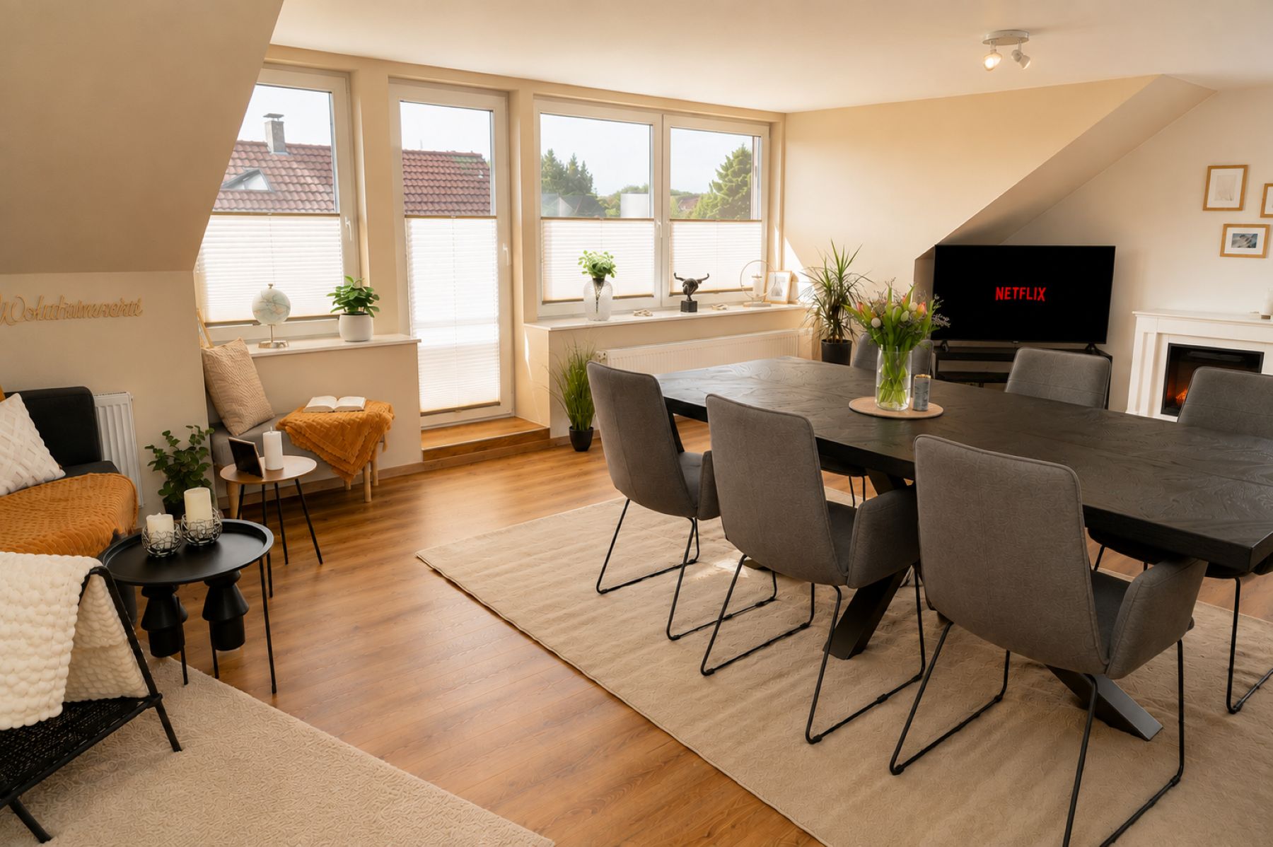 Ein modernes Wohnzimmer mit Essbereich, großen Fenstern, einem Kamin und einem Flachbildfernseher.