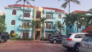 A multi-story building with balconies, parked cars, and palm trees. - 2BR Condo With Pool, Walk to Beach, Bávaro (Punta Cana)