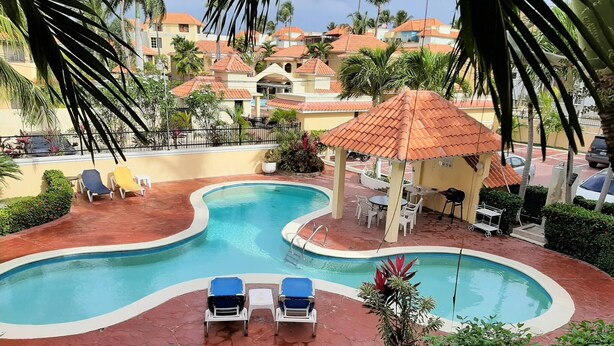 A swimming pool with lounge chairs, a gazebo, and surrounding greenery. - 2BR Condo With Pool, Walk to Beach, Bávaro (Punta Cana)
