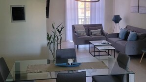 A modern living room with a glass dining table, two sofas, a coffee table, and a hanging light fixture. - 2BR Condo With Pool, Walk to Beach, Bávaro (Punta Cana)