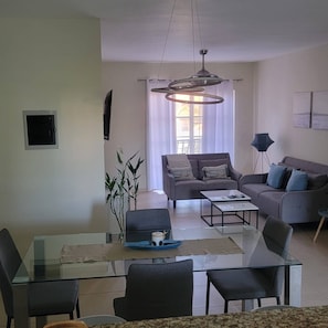 A modern living room with a glass dining table, two sofas, a coffee table, and a hanging light fixture. - 2BR Condo With Pool, Walk to Beach, Bávaro (Punta Cana)
