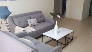 A living room with a grey sofa, a white coffee table, and a blue floor lamp. - 2BR Condo With Pool, Walk to Beach, Bávaro (Punta Cana)