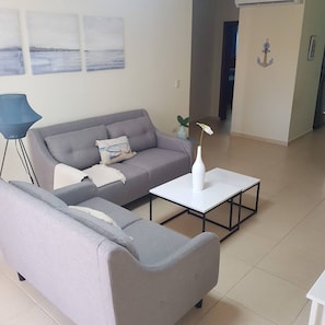 A living room with a grey sofa, a white coffee table, and a blue floor lamp. - 2BR Condo With Pool, Walk to Beach, Bávaro (Punta Cana)